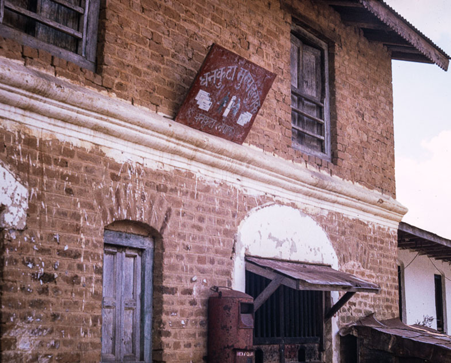 A weathered brick building with a hand-painted Nepali signboard